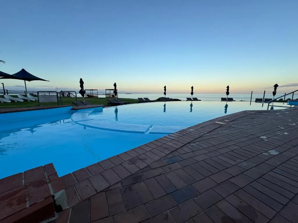 Scenic infinity pool overlooking ocean at sunrise with loungers and umbrellas