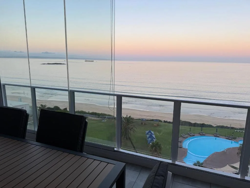 Sunset ocean view with beach and pool visible from modern glass balcony