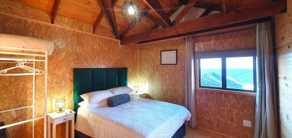 Cozy bedroom with green headboard, wooden beams, and ocean view windows