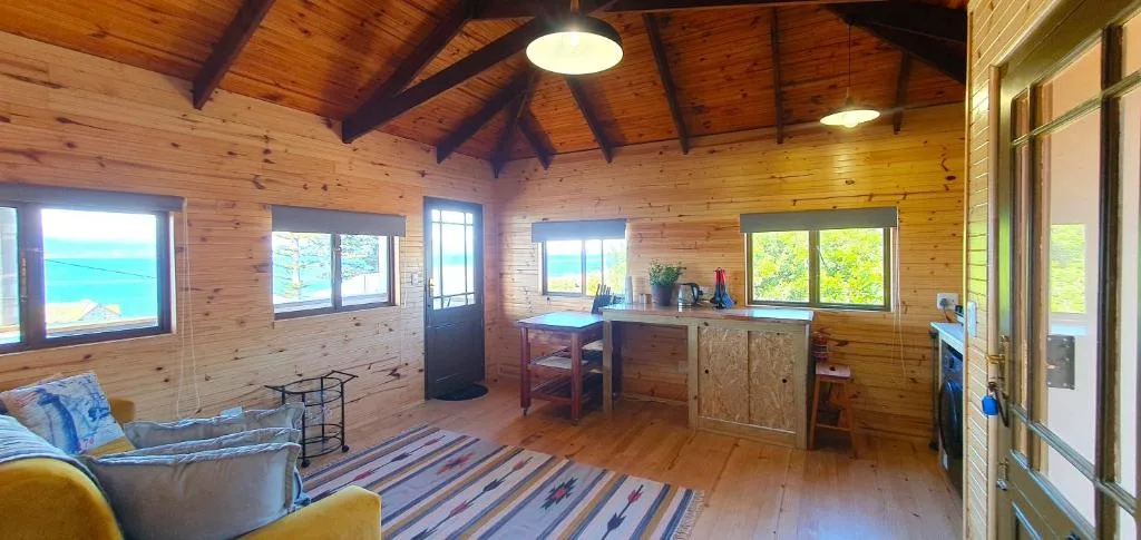 Open-plan lounge with wooden beams, sofa, and ocean views through windows