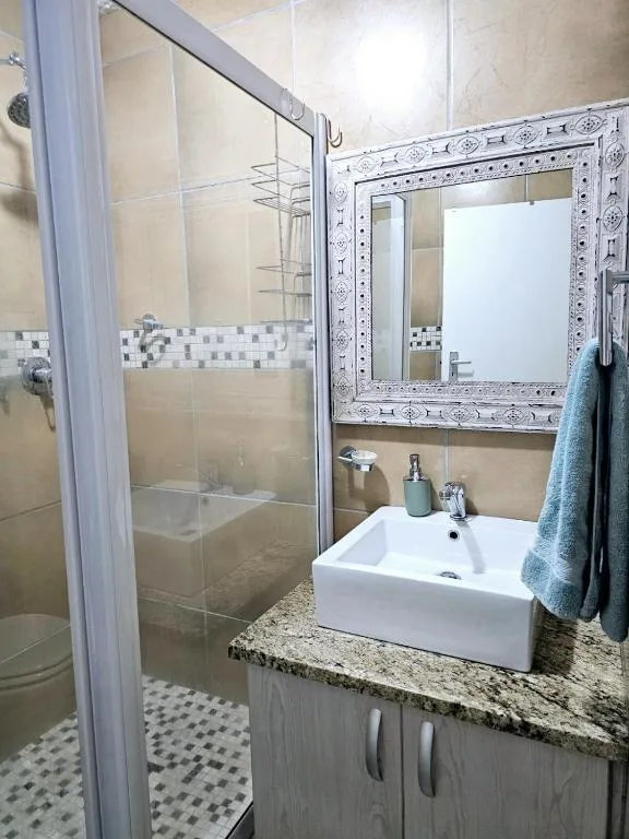Modern bathroom with glass shower, white vanity sink, and decorative mirror