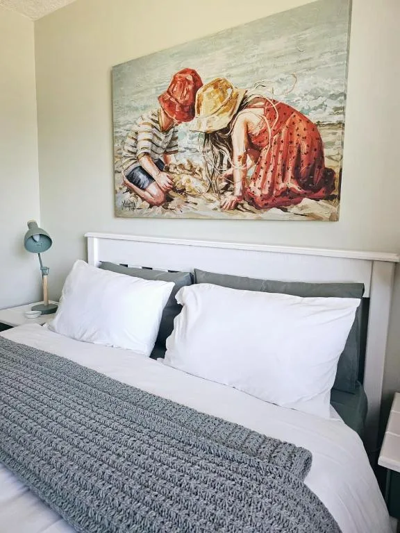 Bedroom with white pillows, gray bedding, and colorful artwork above headboard