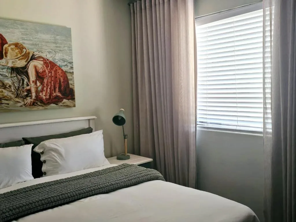 Bright bedroom with white bedding, artwork, curtains, and natural light