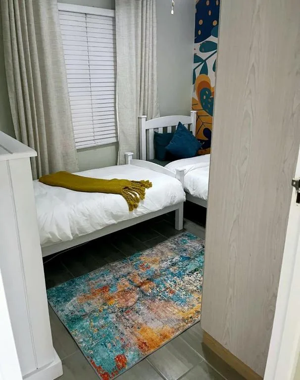 Bright bedroom with white beds, colorful rug, and coastal-themed wall art