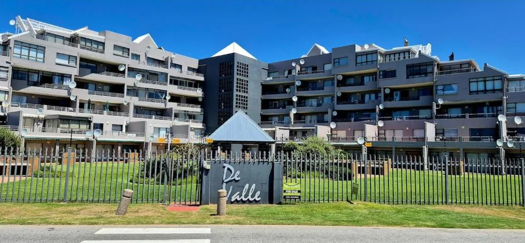 Modern waterfront apartment complex with De Valle signage and manicured lawn