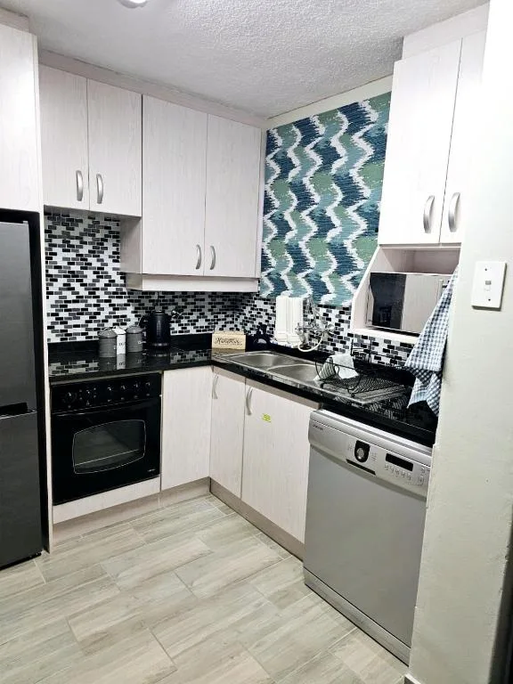 Modern kitchen with white cabinetry, black and white mosaic backsplash, stainless steel appliances
