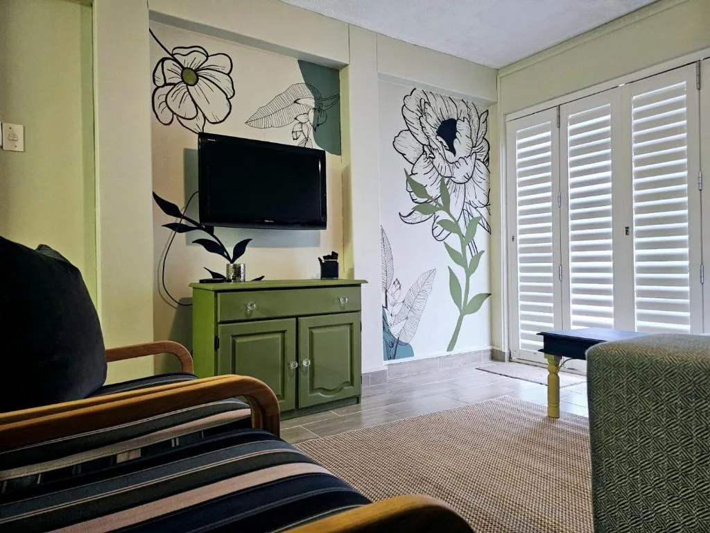 Modern lounge with TV, green cabinet, botanical wall art, and shuttered doors