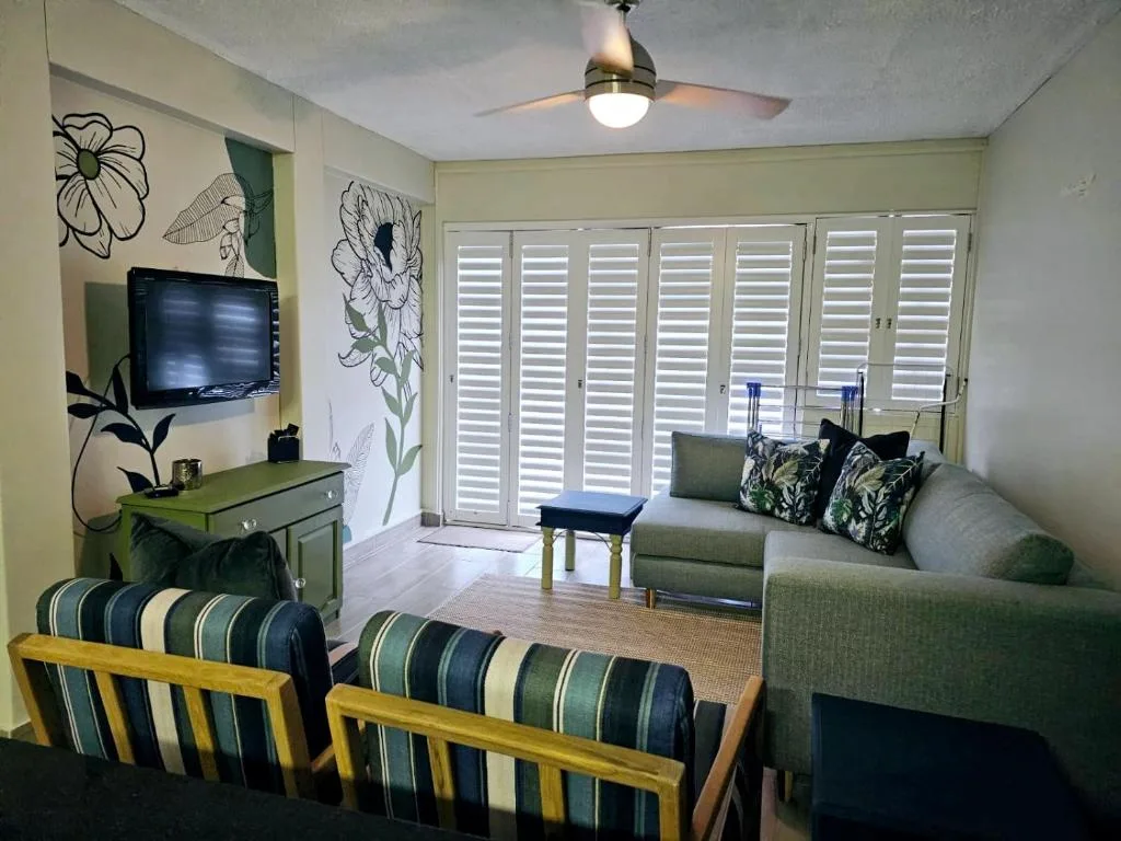 Bright living room with green sofa, striped armchairs, wall-mounted TV, and botanical artwork