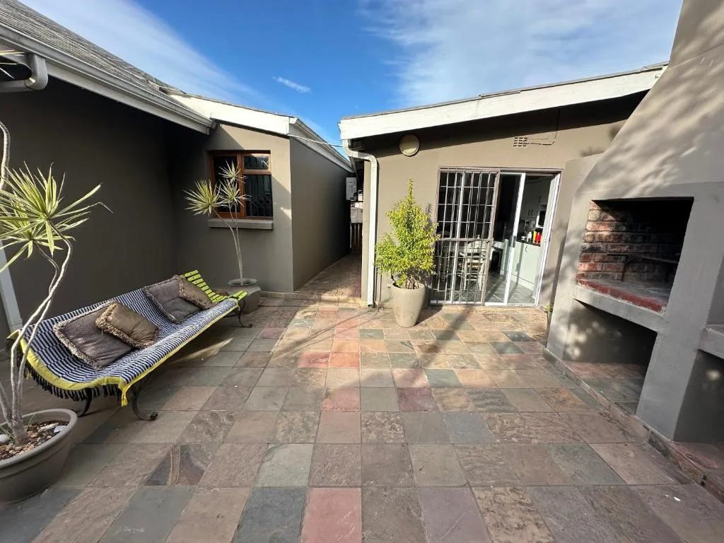 Paved courtyard with lounging area, potted plants, and braai fireplace