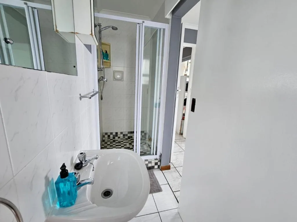 Modern bathroom with white sink, shower enclosure, and black-and-white floor tiles
