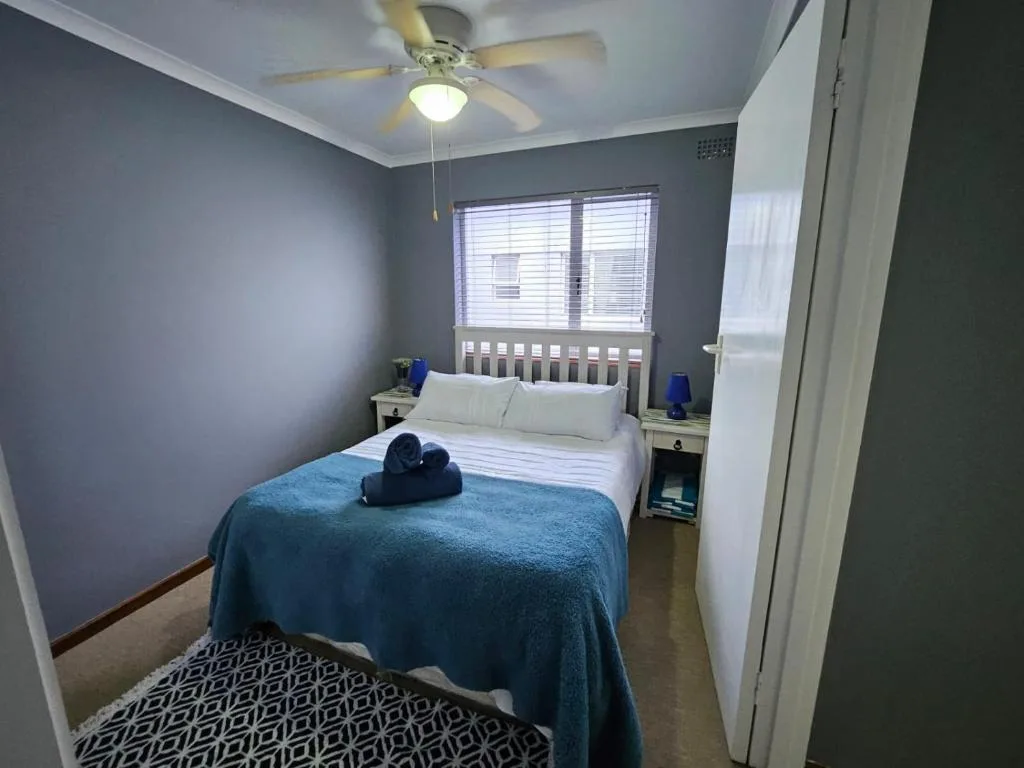 Bright bedroom with queen bed, blue throw, ceiling fan, and natural light