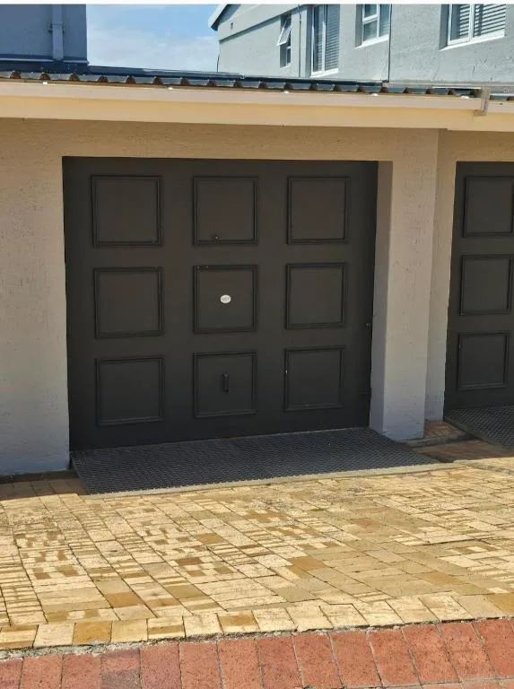 Black panelled garage door on cream render wall with paved driveway