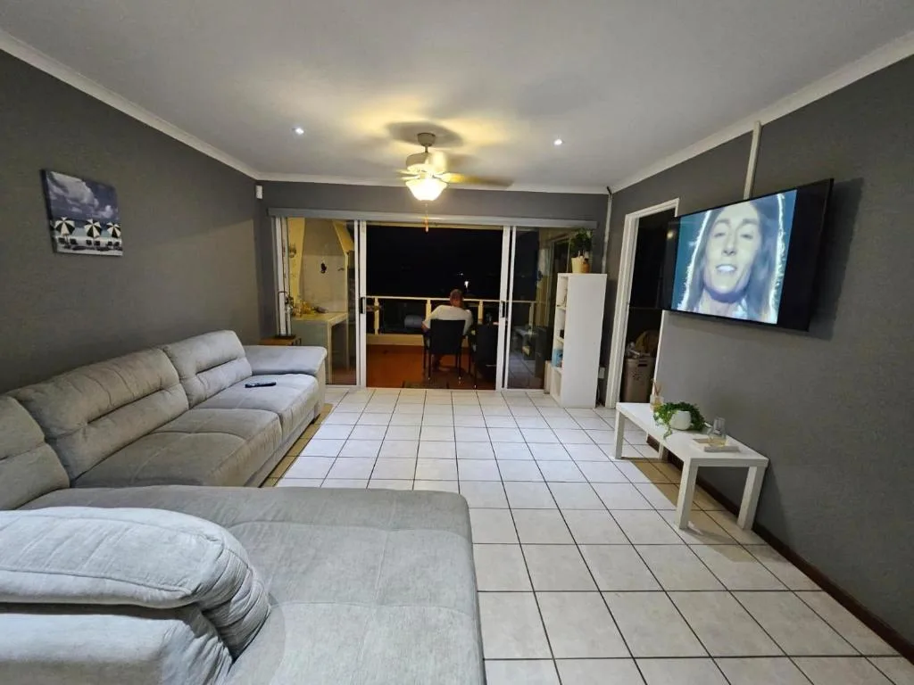 Modern lounge with gray sofas, wall-mounted TV, and deck access at dusk