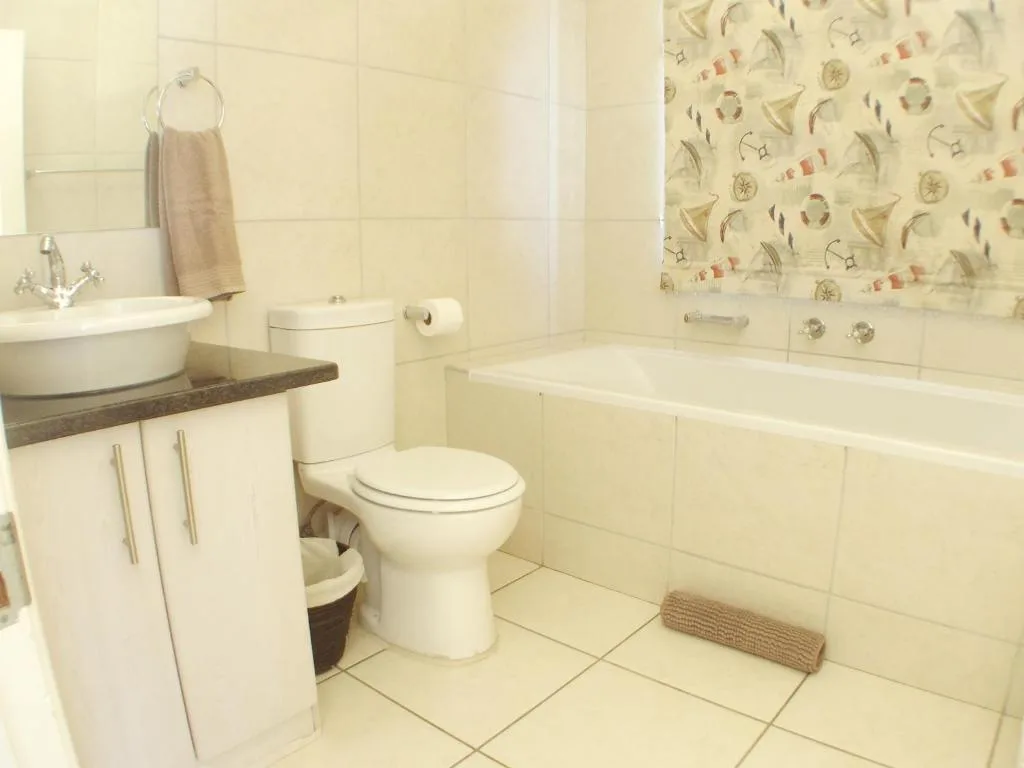Clean bathroom with round sink, toilet, bathtub, and nautical-themed wallpaper