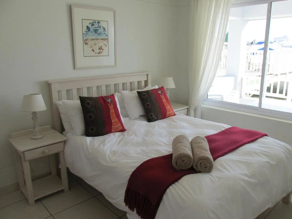 Bright bedroom with white bed, burgundy accents, and ocean view through sliding doors