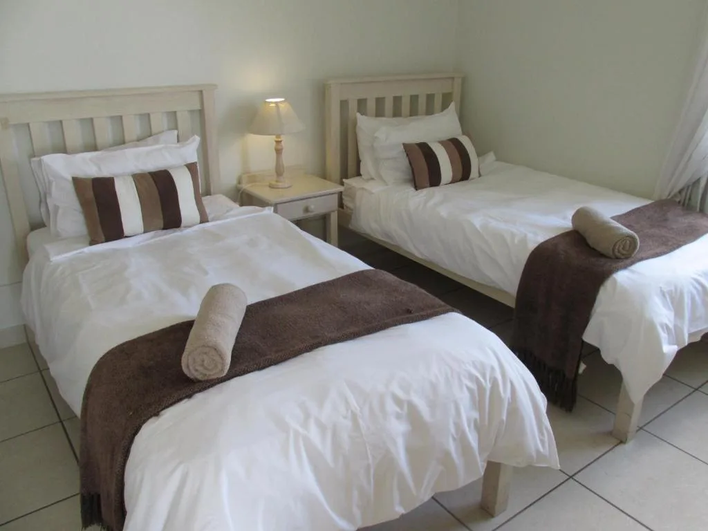 Twin bedroom with white linens, brown accents, and bedside lamp