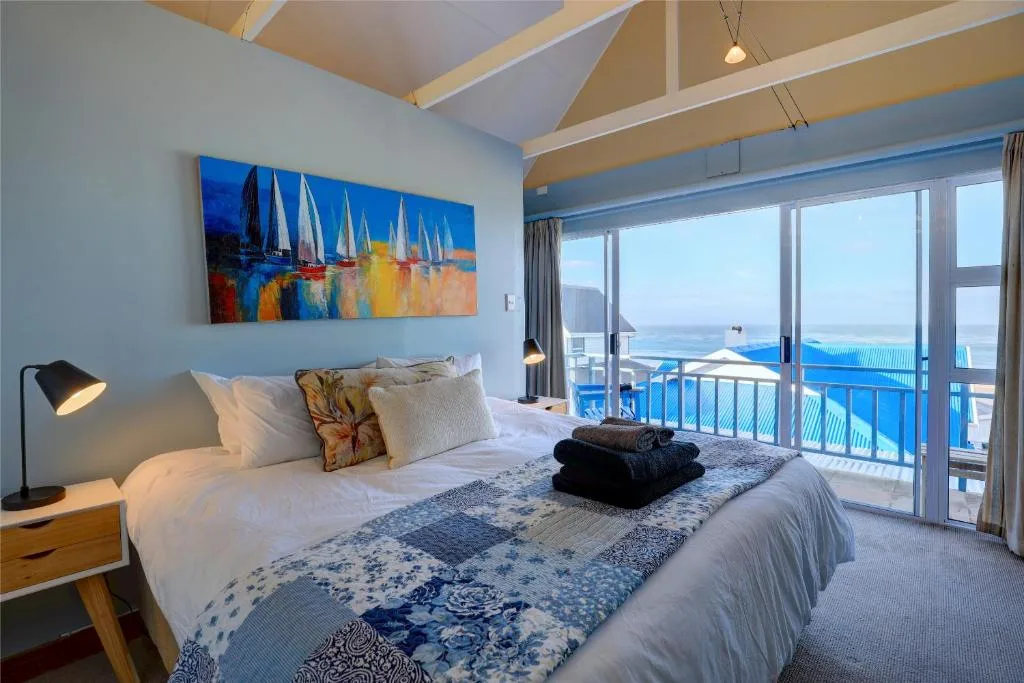 Bright bedroom with ocean view through glass doors and sailing artwork