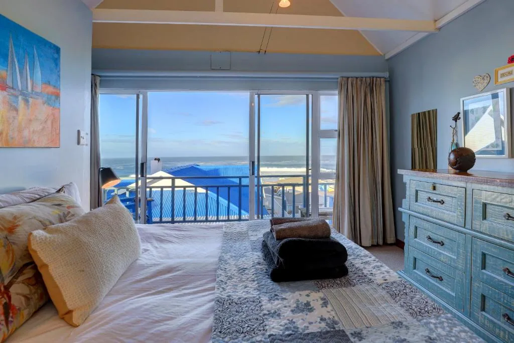 Spacious bedroom with ocean view, bed, and blue balcony railing visible