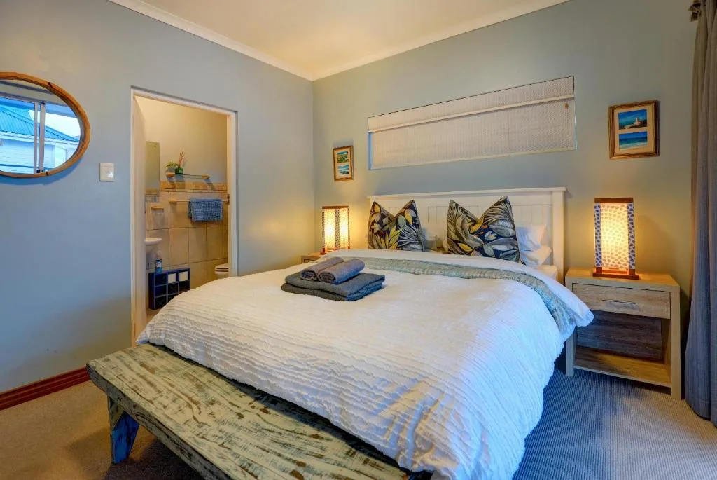 Bright bedroom with white bed, colorful pillows, and ensuite bathroom visible