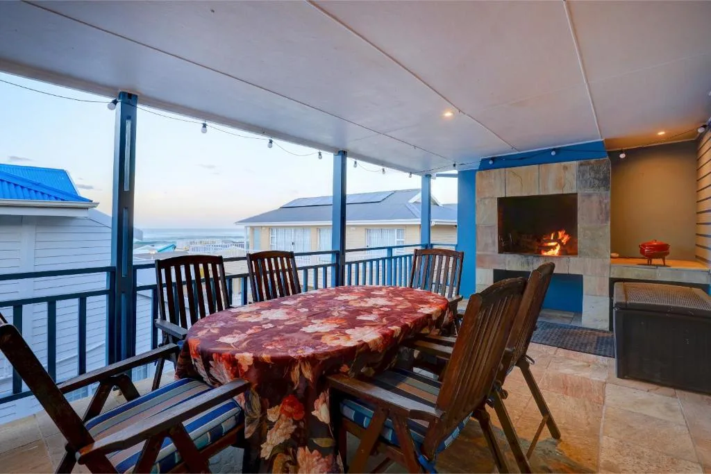 Covered deck with dining table, fireplace, and panoramic ocean views at dusk