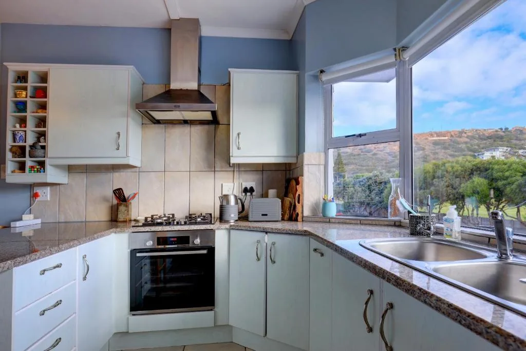 Modern kitchen with white cabinetry, granite counters, and hillside views through window