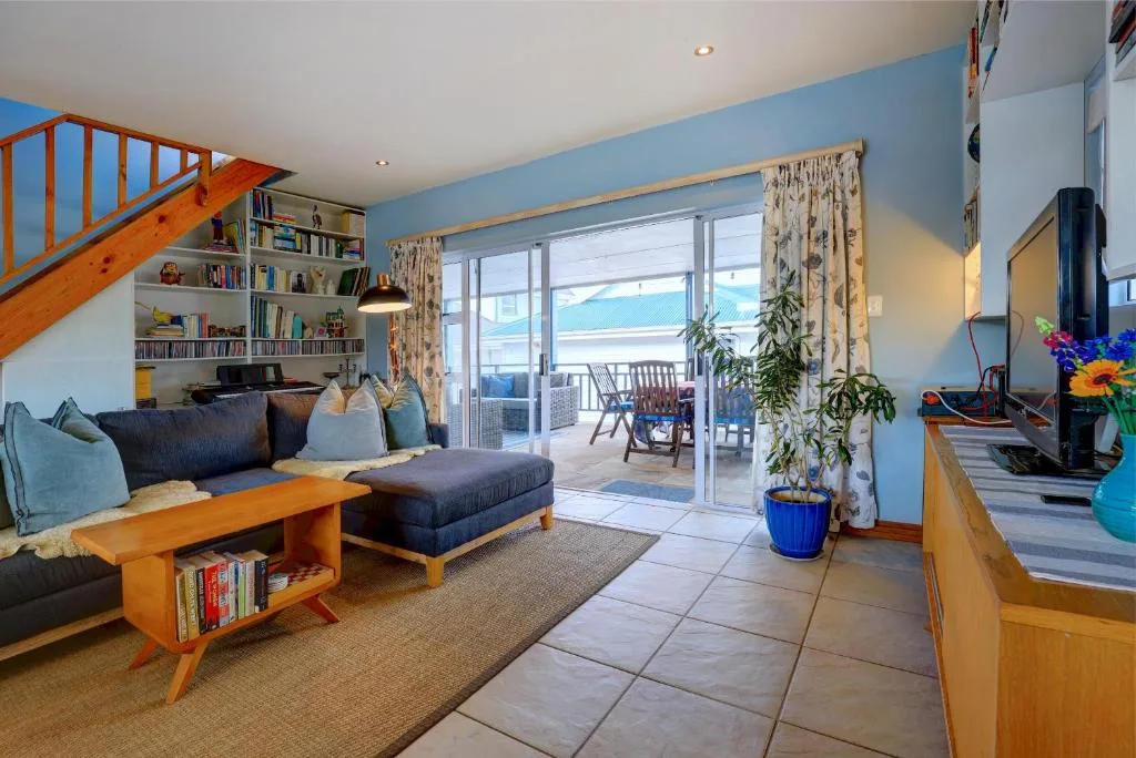 Bright lounge with blue walls, dark sofa, wooden coffee table, and ocean view through glass doors