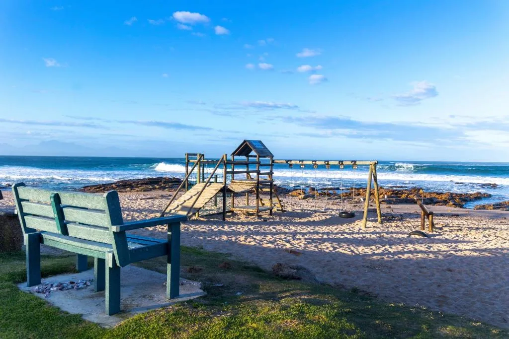 Beach view with playground and blue bench overlooking ocean waves