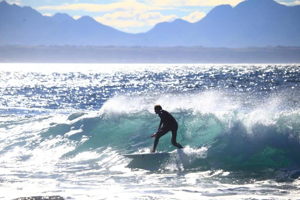 Surfer riding wave with mountains and sparkling ocean backdrop