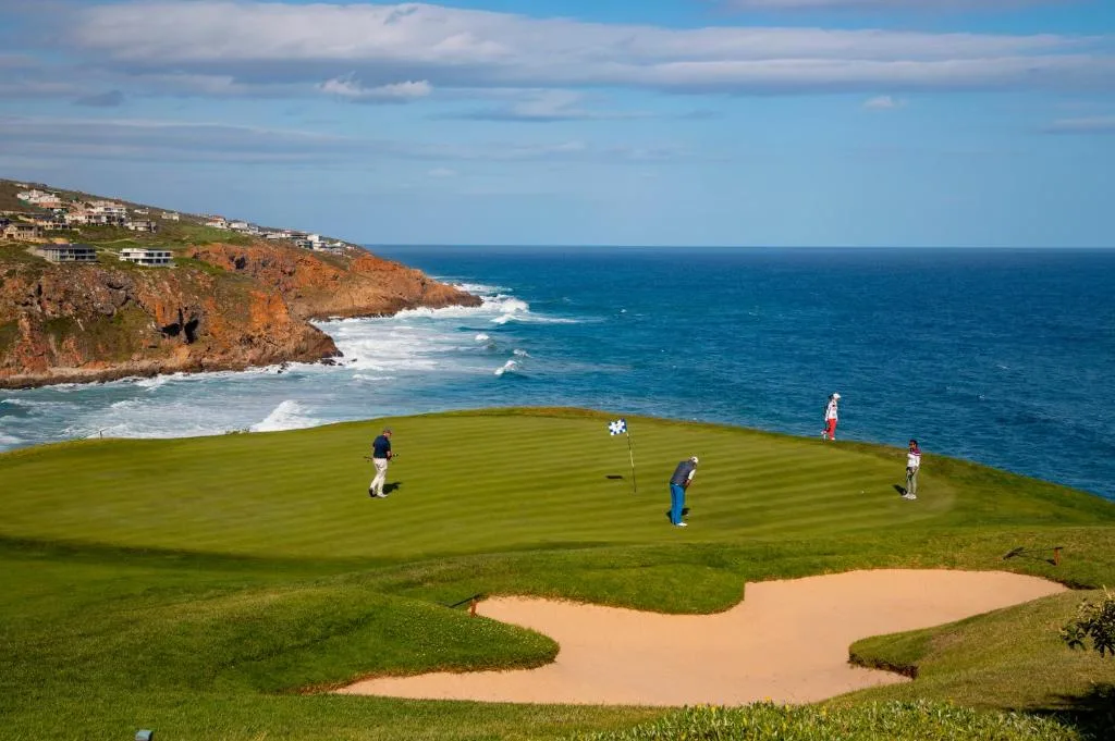 Dramatic coastal golf course with ocean cliffs, waves, and seaside properties visible