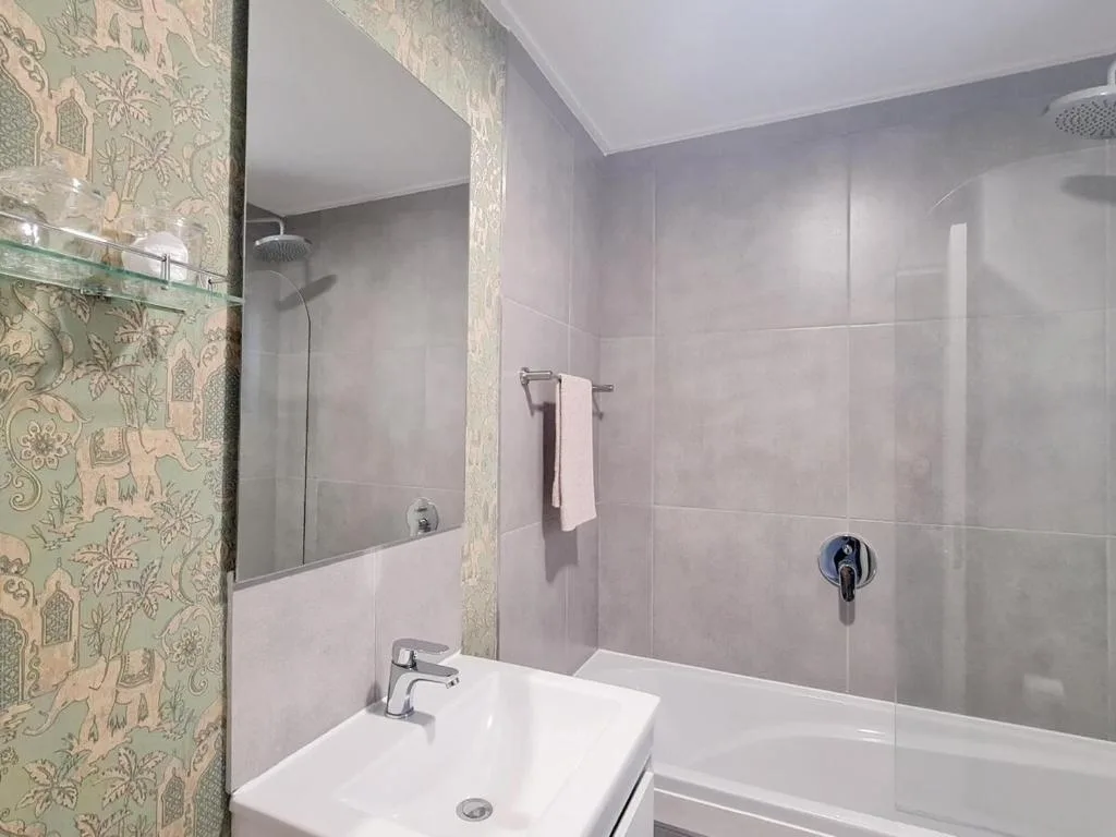 Modern bathroom with grey tiles, vanity sink, and enclosed shower