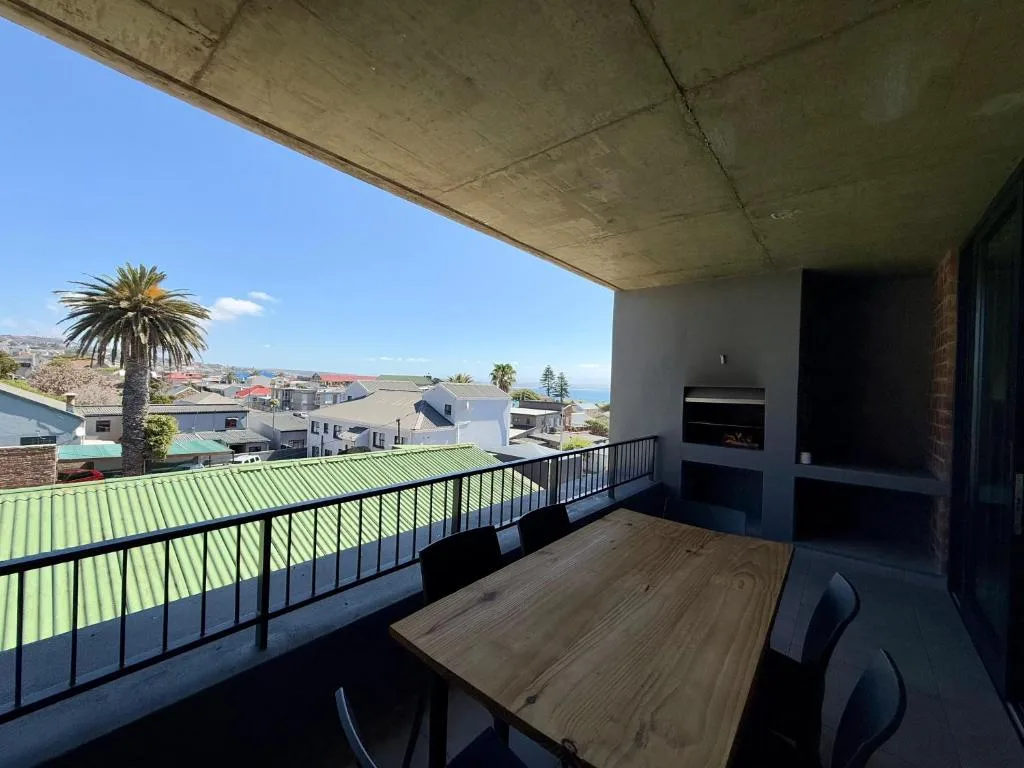 Spacious outdoor balcony with dining table overlooking coastal town and ocean