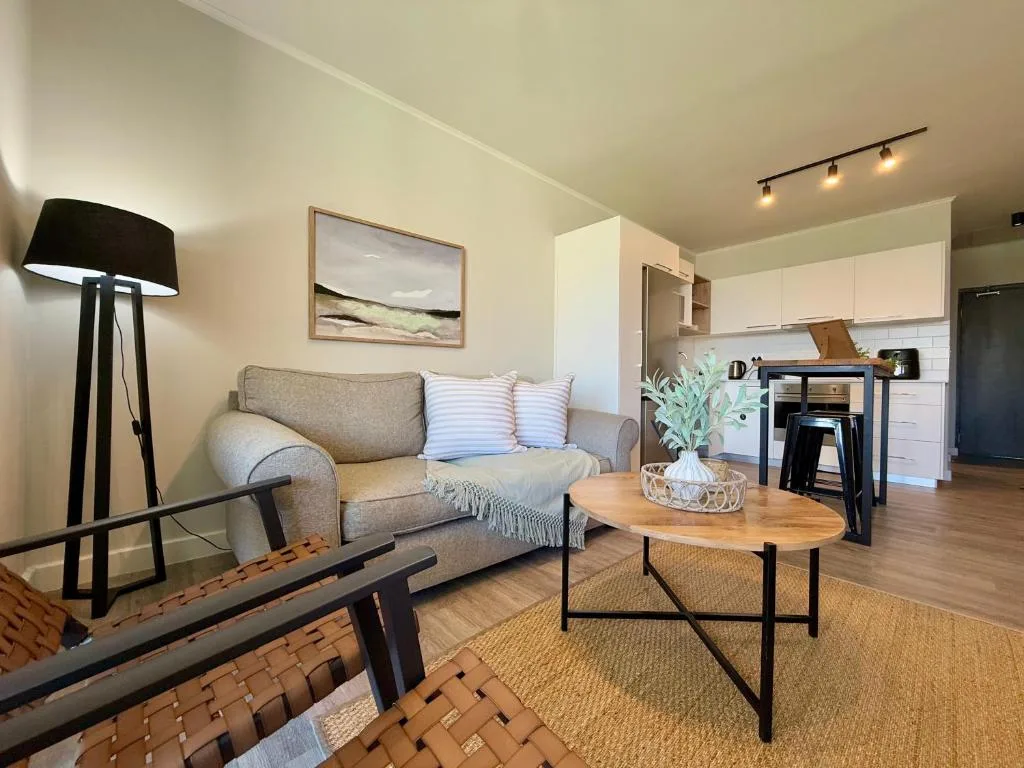 Open-plan lounge with grey sofa, wooden coffee table, and kitchen beyond