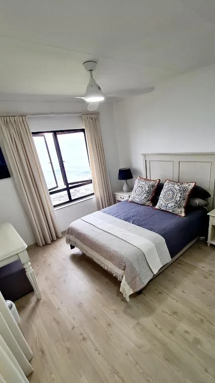 Bright modern bedroom with queen bed, patterned pillows, and ocean view.
