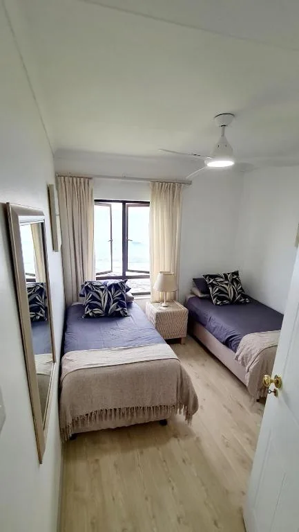 Bright bedroom with two beds, mirrored wardrobe, and ocean view windows
