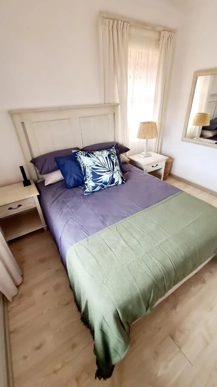 Bedroom with queen bed, purple bedding, decorative pillows, and bedside table