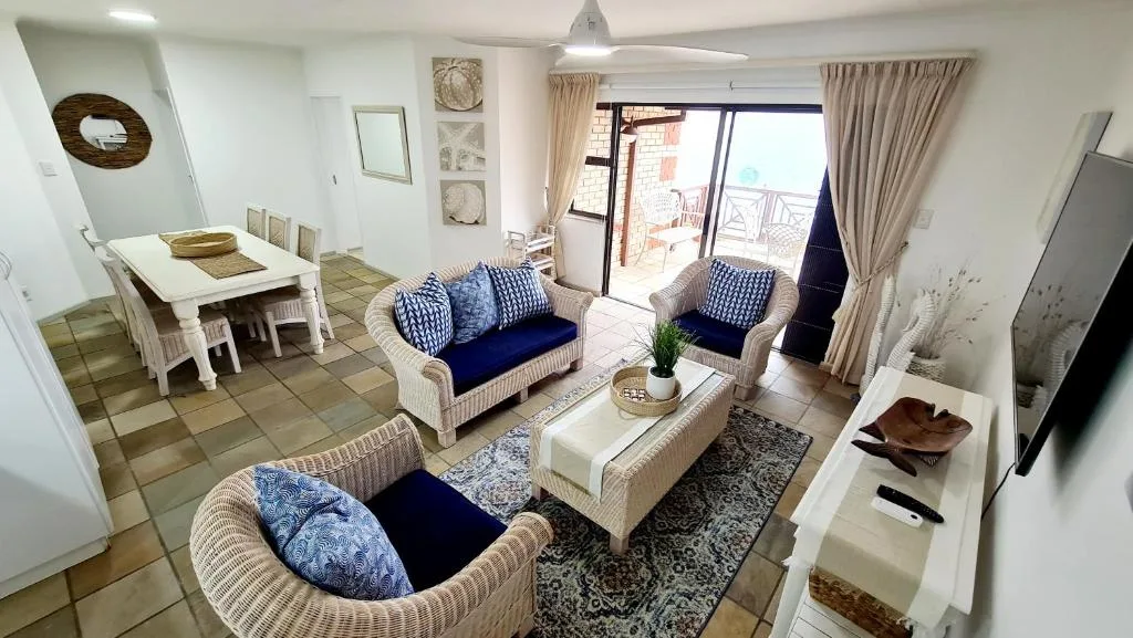 Open-plan lounge with wicker seating, blue cushions, and ocean view doors