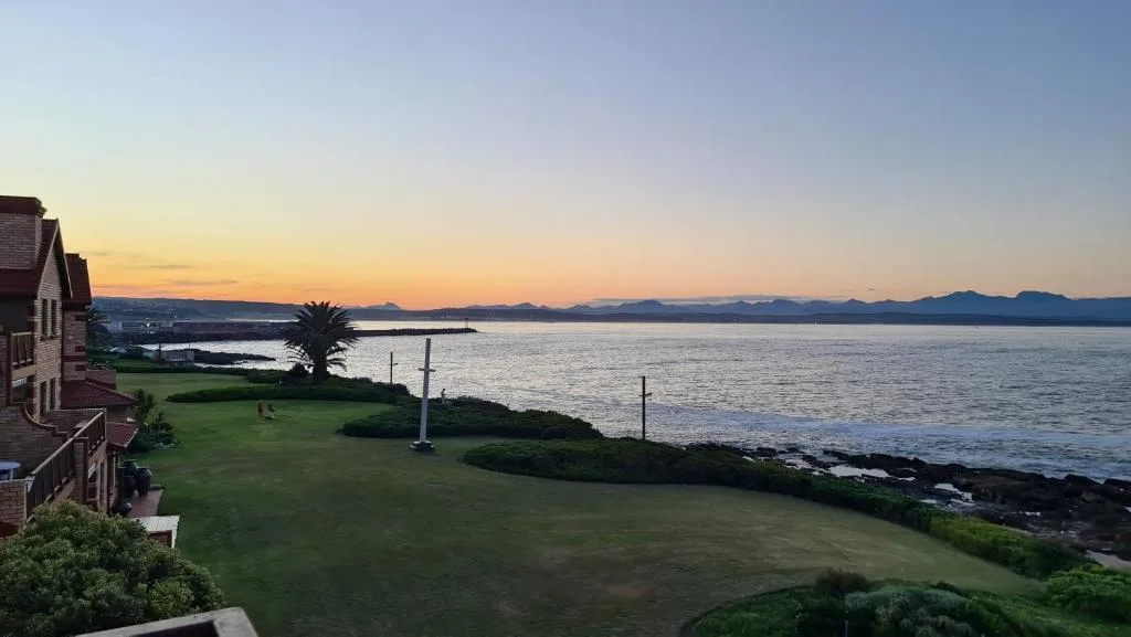 Sunset over ocean with mountains, lush garden lawn and palm tree