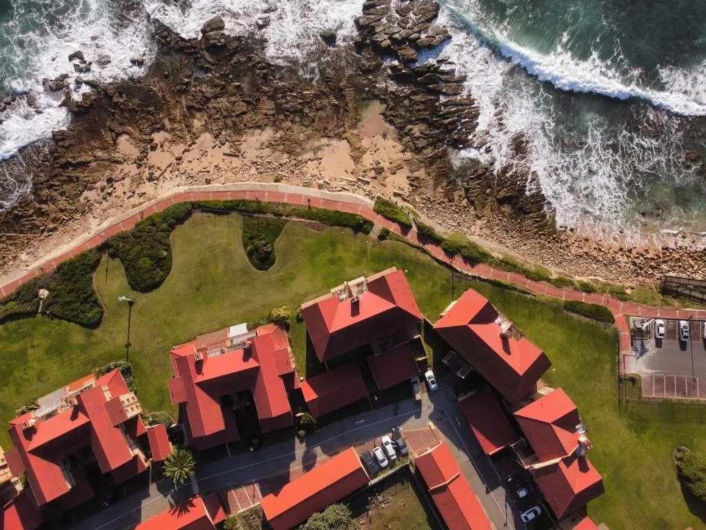 Aerial view of beachfront property with red-roofed buildings and crashing ocean waves