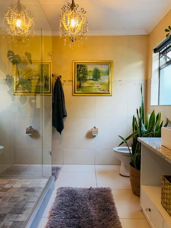Modern bathroom with walk-in shower, ornate chandelier, artwork, and potted plants