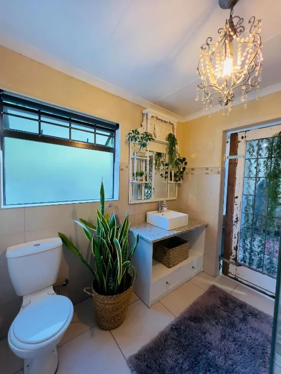 Bright bathroom with toilet, vanity sink, decorative plants, chandelier