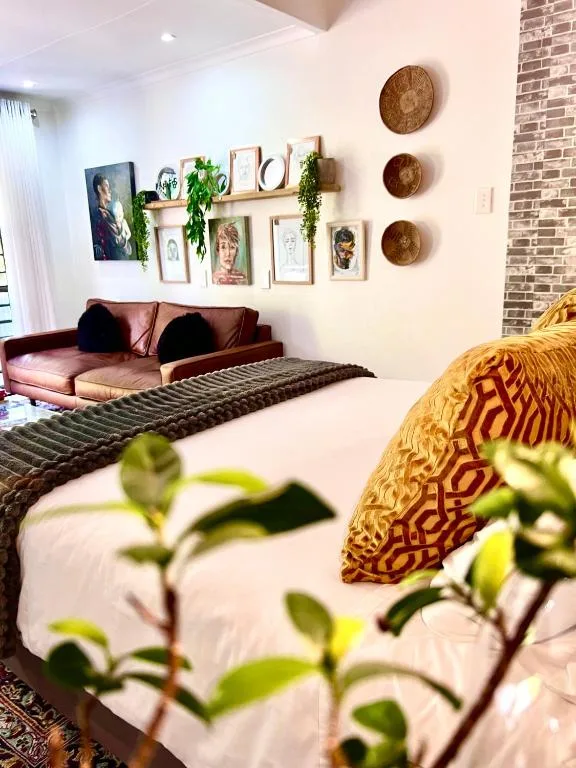 Modern bedroom with burgundy sofa, gallery wall art, woven baskets, and potted plants
