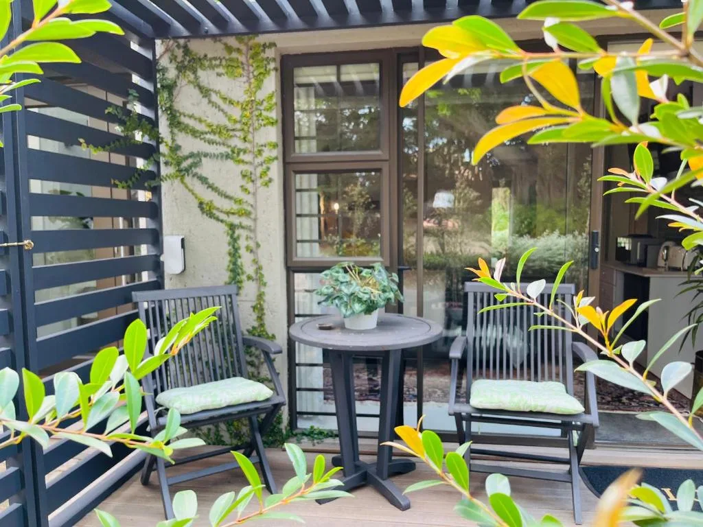 Modern outdoor patio with comfortable seating, small table, and lush yellow flowering plants