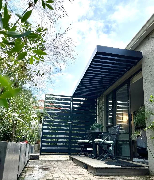 Modern patio with black pergola, seating area, and lush garden surroundings