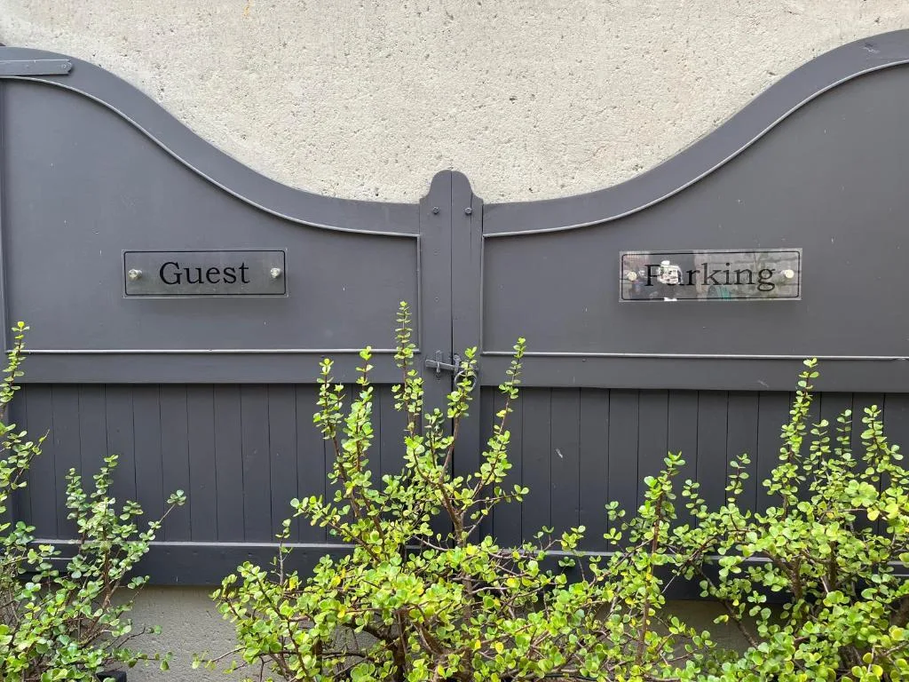 Black driveway gate with guest and parking signs, green climbing vines