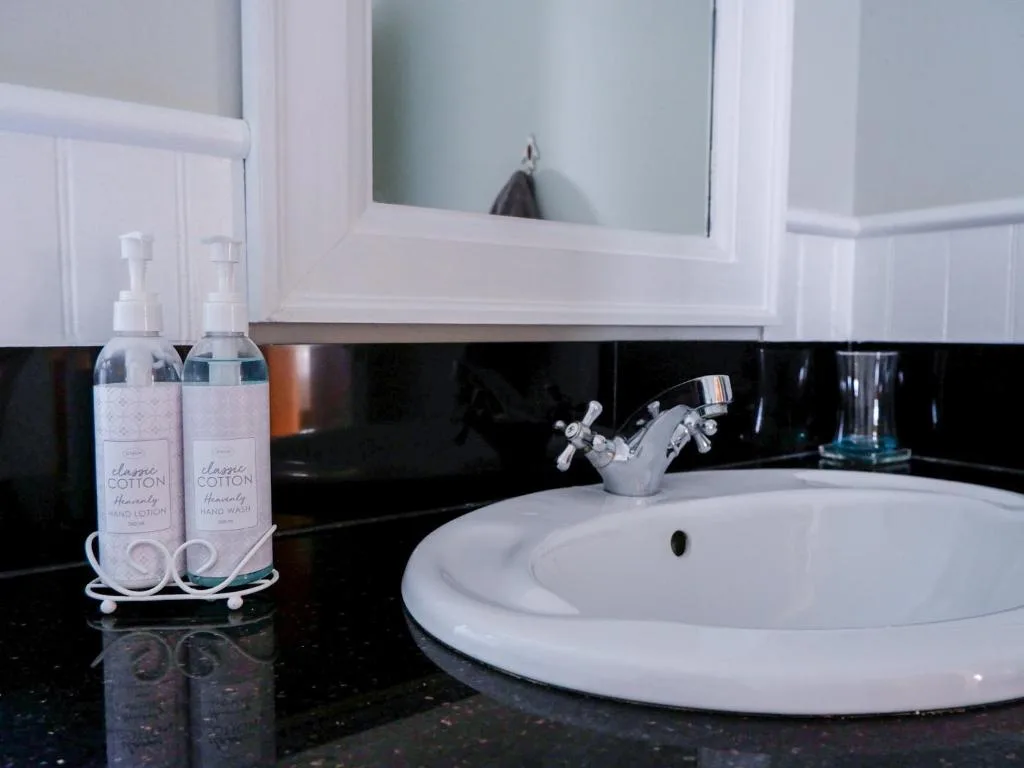 Modern bathroom with round white sink, black backsplash, and cotton toiletries