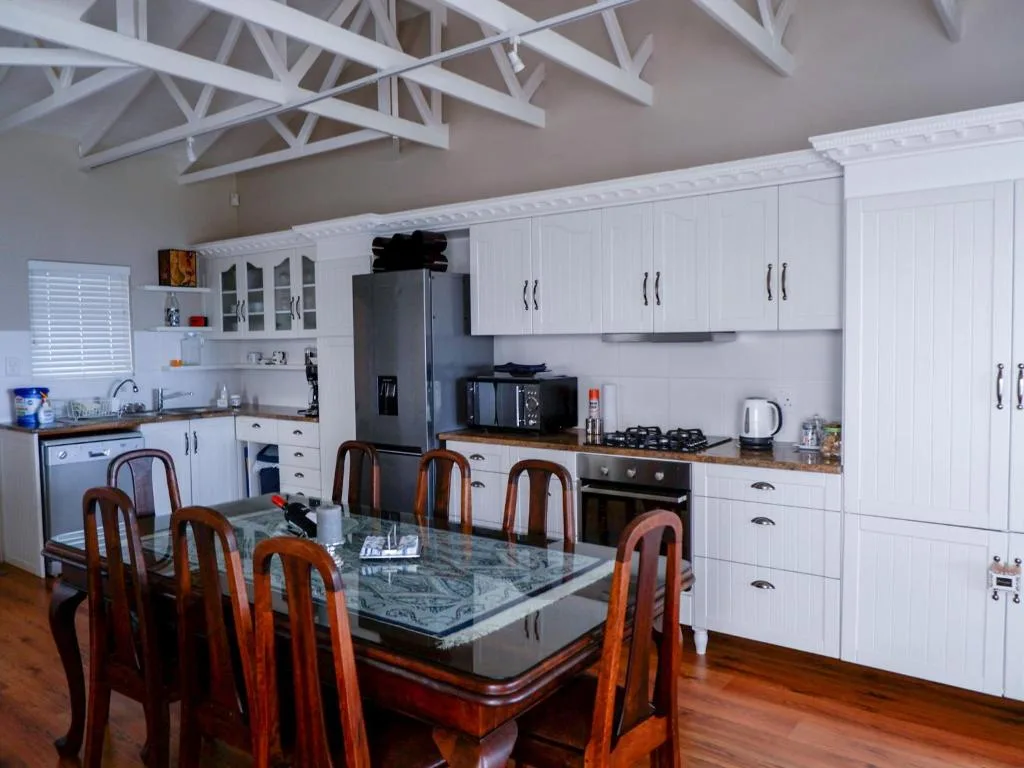 Modern white kitchen with dining table, black appliances, and wooden chairs