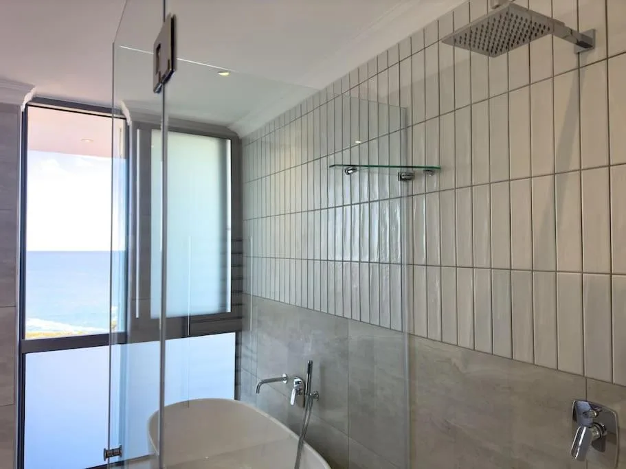 Modern bathroom with rainfall showerhead, tiled walls, and ocean view window