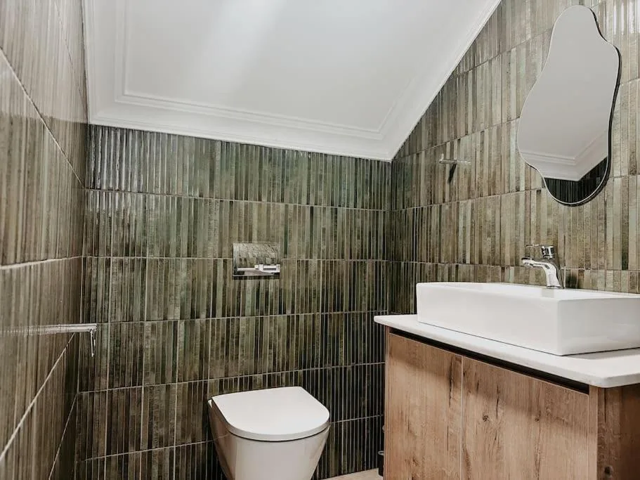 Modern bathroom with green tile walls, white vessel sink, and toilet