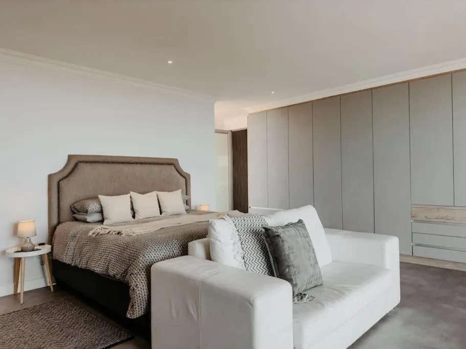 Spacious master bedroom with upholstered bed, modern wardrobe, and seating area