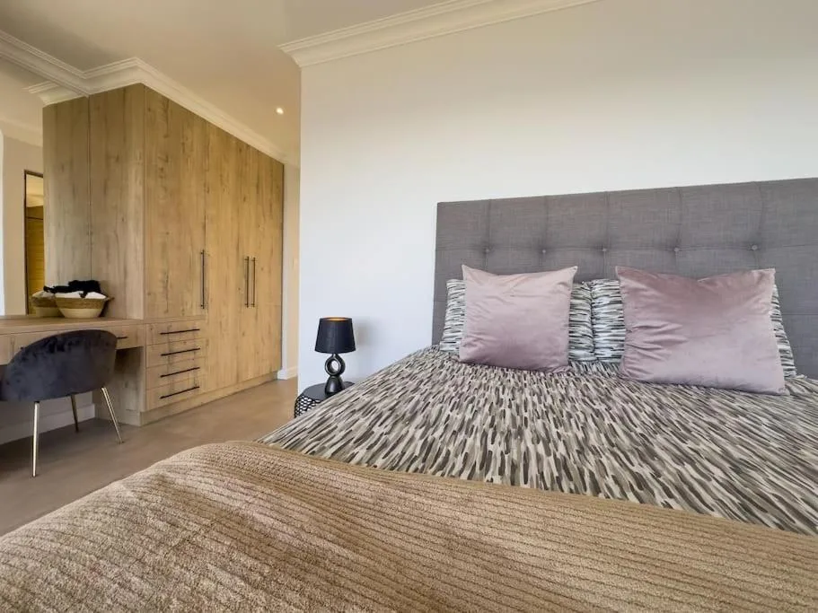 Spacious bedroom with gray upholstered bed, pink pillows, and wooden wardrobe